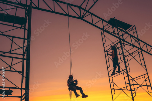 Silhouette of engineer and construction team working safely on scaffolding on high rise building. over blurred background sunset pastel for industry background with Light fair