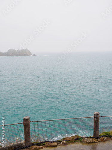 Wide vertical view of a fenced walkway long the tall cliffs of Porthcurno beach. Cornwall, United Kingdom. Travel and nature.