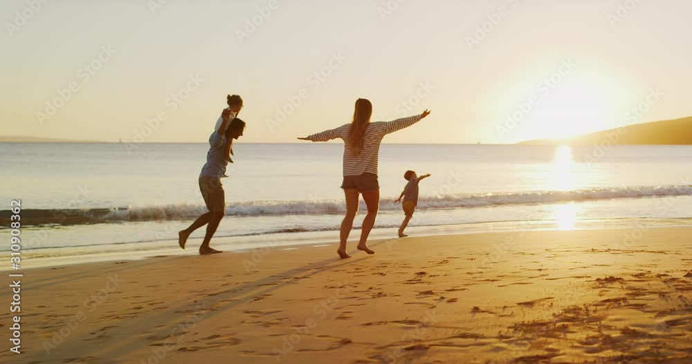 Happy family with young children running and flying into the sunset at the beach, family fun at the beach, joyful parenthood moments