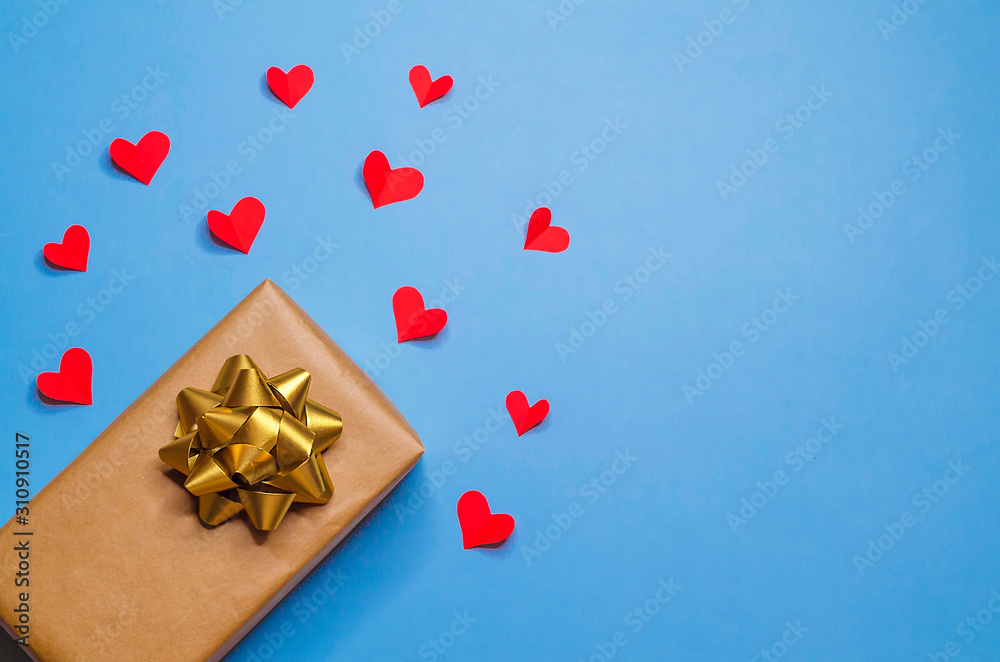 universal gift in package with gold bow and red hearts in recognition of love on trendy blue background for New Year, Christmas, Valentines Day, birthday. copy space universal gift in package with gold bow and red hearts in recognition of love on trendy blue background for New Year, Christmas, Valentines Day, birthday. copy space