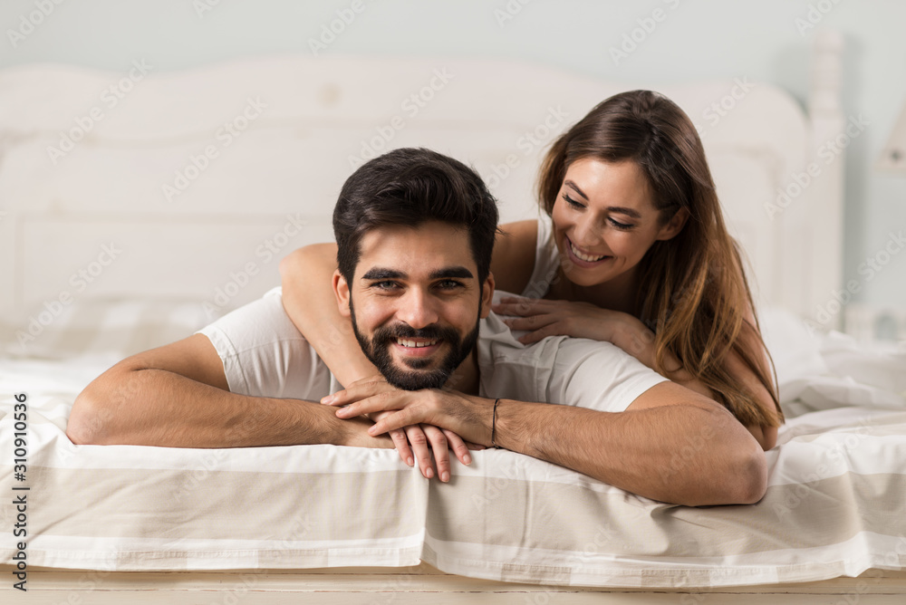 Obraz premium Beautiful couple relaxing together on a bed at home. Man is looking at camera