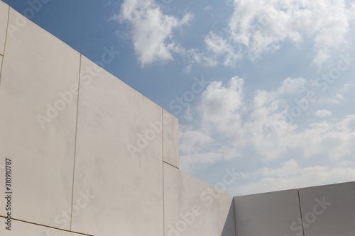 Modern architecture. Big white walls of the building against the blue sky and white clouds. Minimalistic design