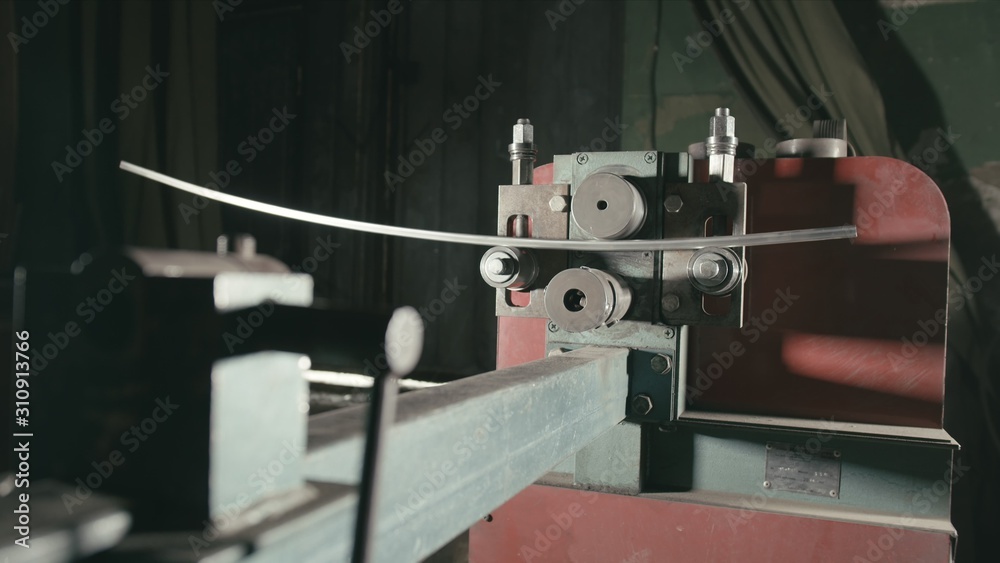 Fototapeta premium Forge workshop on table. Smithy manual production. Worker bends the metal rod on the wrought iron round bending machine. Manufacturing of a designer part from a metal rod. The blacksmith manufacture.
