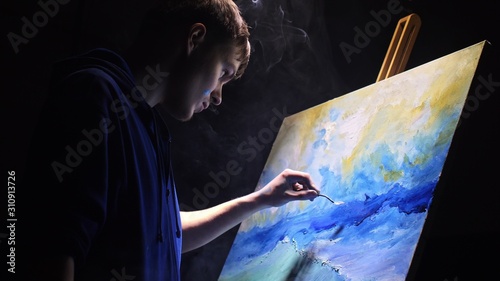 Artist copyist paint seascape with ship in ocean. Vaper smoke vape e-cigarette. Craftsman decorator draw as boat sail on blue sea with acrylic oil color. Draw finger, brush, knife palette. Indoor. photo