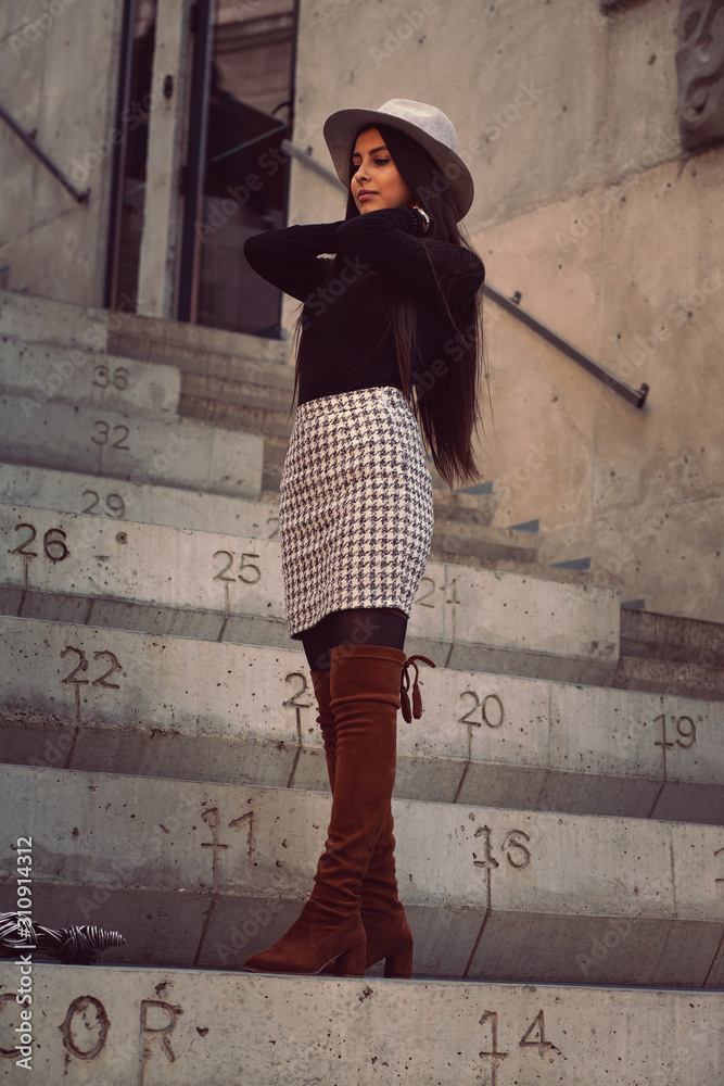 stylish girl in a hat with long hair posing on the steps of the building