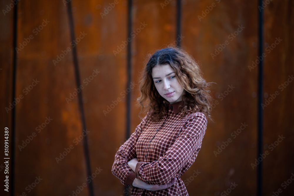 Fototapeta premium Dreaming young woman with spectacular curly red ginger hair looking at camera posing outdoor in downtown street. Female portrait.