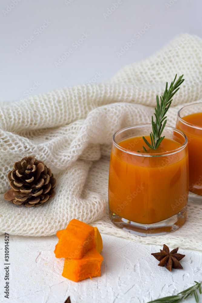 Fresh drinking. winter decoration. cocktail with sprig of rosemary with the warm white plaid on white table.glass of fresh pumpkin or oranges juice with slices of pumpkin, spices. vertical orietation
