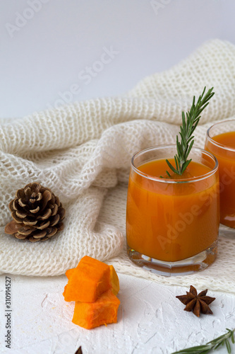 Fresh drinking. winter decoration. cocktail with sprig of rosemary with the warm white plaid on white table.glass of fresh pumpkin or oranges juice with slices of pumpkin, spices. vertical orietation photo