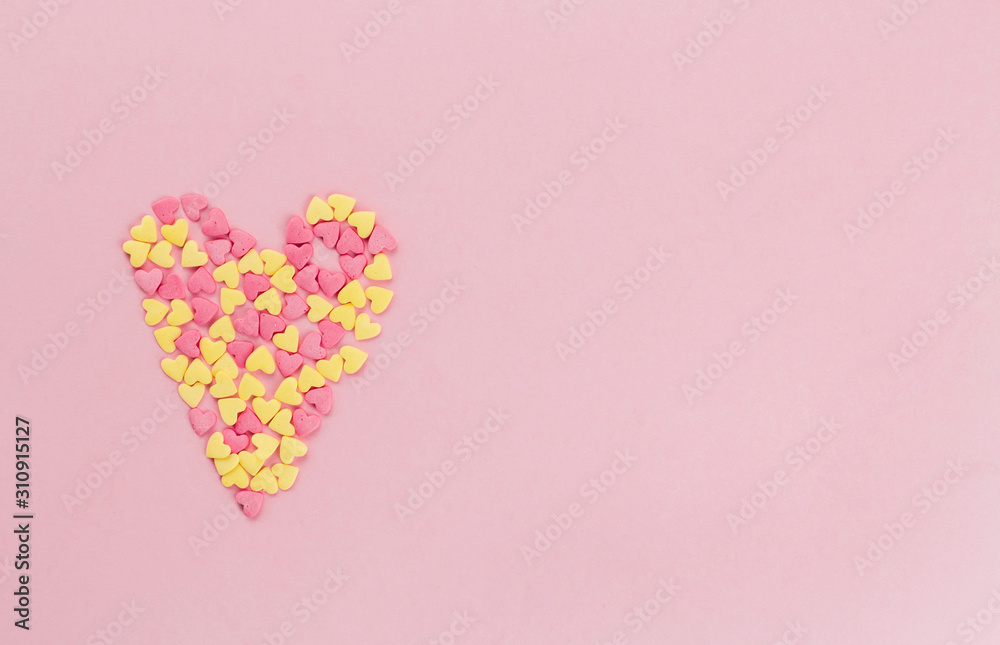  heart of pink and yellow confetti confectionery on a pink background copy space.