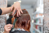 Woman getting a new haircut. Female hairstylist cutting hair with scissors in hair salon. Hairdresser hold in hand between fingers lock of hair, comb and scissors closeup.