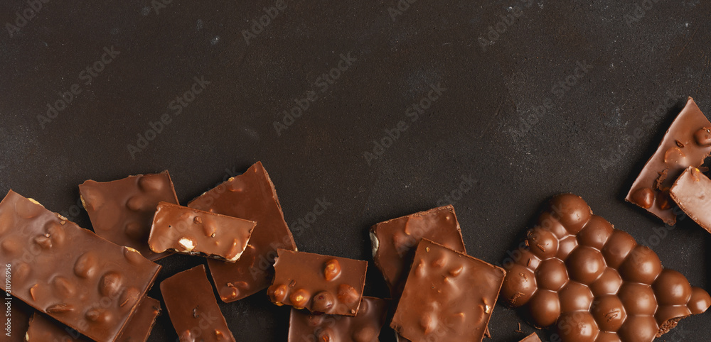 The chunks of broken different chocolate bars with nuts on the black stone surface with space for text. Background with chocolate. Sweet food photo concept. The chunks of broken different chocolate bars with nuts on the black stone surface with space for text. Background with chocolate. Sweet food photo concept.