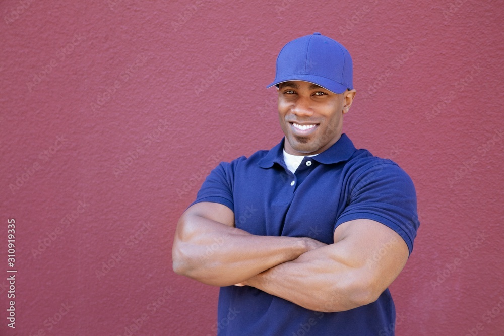 Portrait of a muscular African American delivery man with arms crossed over colored background