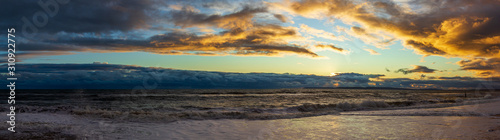 A view of a stony beach at sunset with crashing waves and ecume under a majestic yellow cloudy stormy sky
