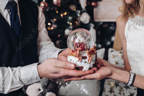 Close-up hands of couple male and female holding statuette of Santa Claus with deer surrounded by snowflakes. Happy family enjoying fairytale Merry Christmas and Happy New Year time