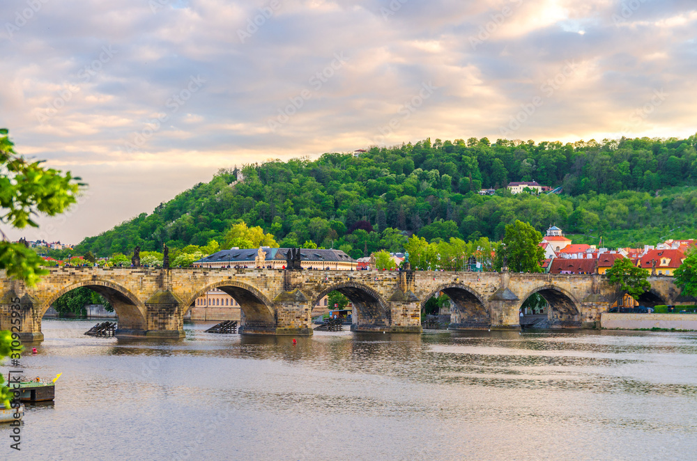 Charles Bridge Karluv Most with alley of dramatic baroque statues over Vltava river in Old Town of Prague historical center, garden on slope of Petrin Hill background, Czech Republic, Bohemia, Europe