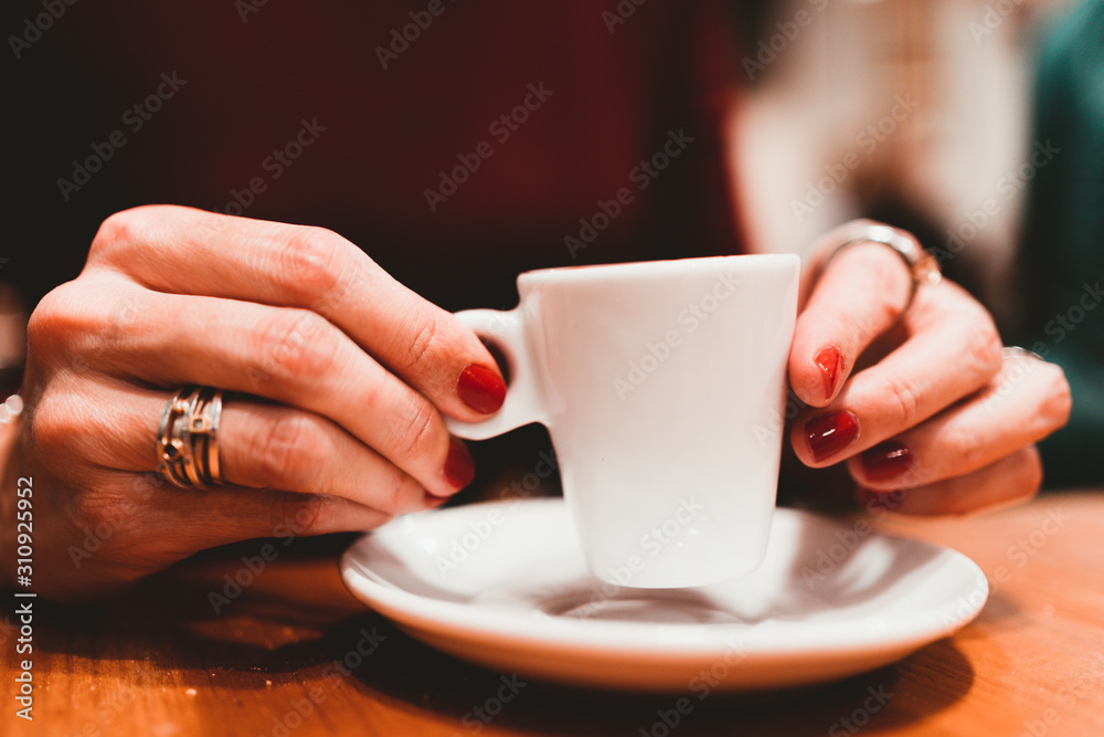 Woman holding in hands cup of coffee on wooden table in cafe. Close up. Woman holding in hands cup of coffee on wooden table in cafe. Close up.