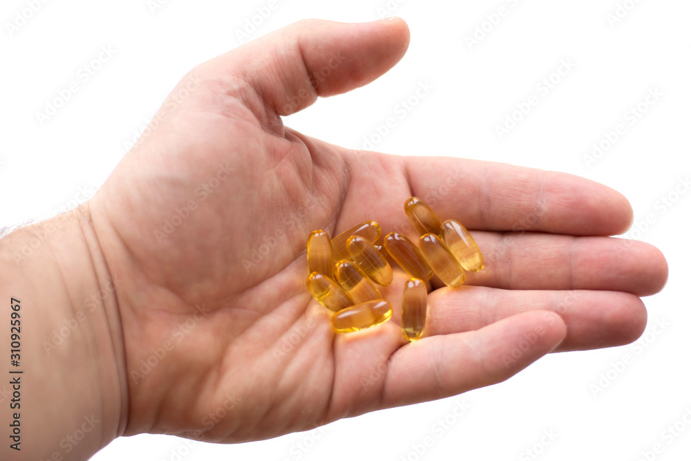 Fototapeta premium A man holds in his hand several fish oil capsules. Omega 3 and vitamin D pills. Healthy lifestyle. Selective focus. Side view.