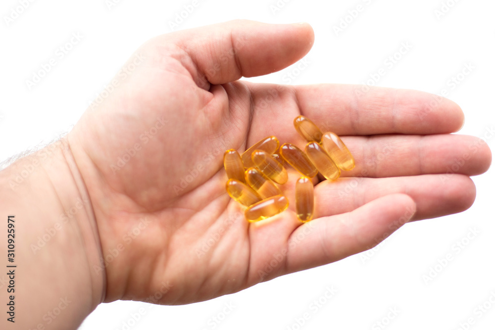 A man holds in his hand several fish oil capsules. Omega 3 and vitamin D pills. Healthy lifestyle. Selective focus. Side view. A man holds in his hand several fish oil capsules. Omega 3 and vitamin D pills. Healthy lifestyle. Selective focus. Side view.