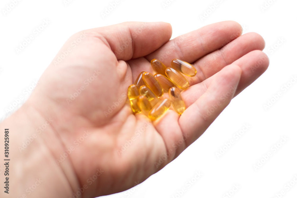 A man holds in his hand several fish oil capsules. Omega 3 and vitamin D pills. Healthy lifestyle. Selective focus. Side view. A man holds in his hand several fish oil capsules. Omega 3 and vitamin D pills. Healthy lifestyle. Selective focus. Side view.