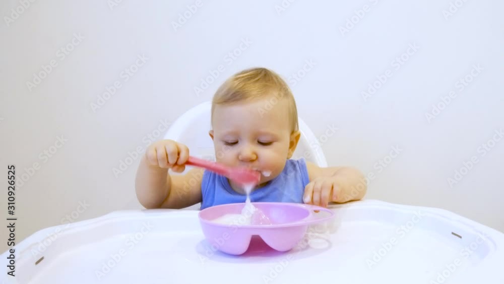 A child for the first time in his life eats porridge himself. The child eats for the first time on his own