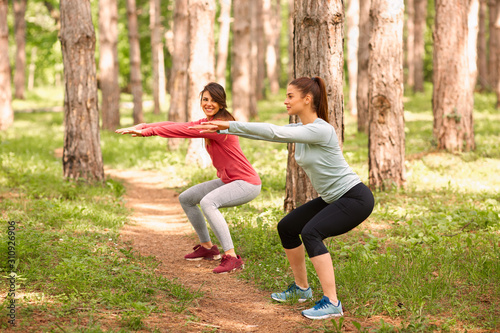 Two best female friends in sportswear doing endurance while squatting. Fitness in nature concept.