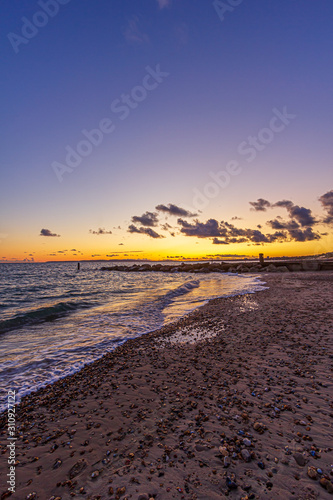 A view of a stony beach at sunset with crashing waves and ecume under a majestic yellow cloudy stormy sky