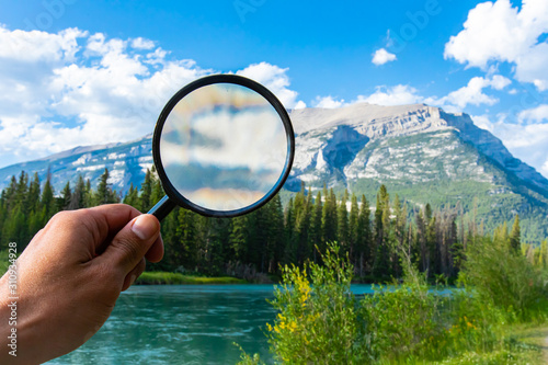 A man is seen using a magnifying glass to take a closer look of a large mountain whilst on vacation in Canmore, Alberta, with copy space to right