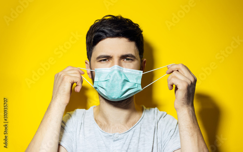 Studio portrait of young ill man, trying to put on, medical flu mask on yellow background.