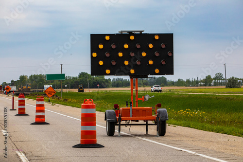 A close up shot of an LED mobile matrix keep left sign, with orange flashing lights warning motorists with arrows and road cones during lane closure