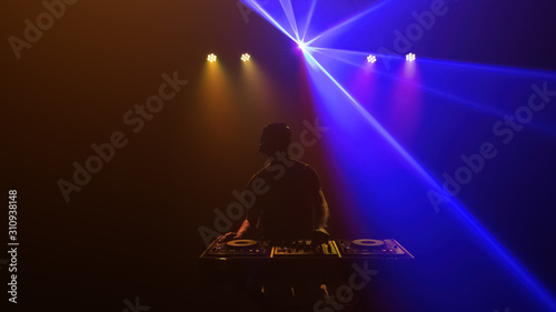DJ - Silhouette of the disc jockey mixing music. Lights and laser of discotheque