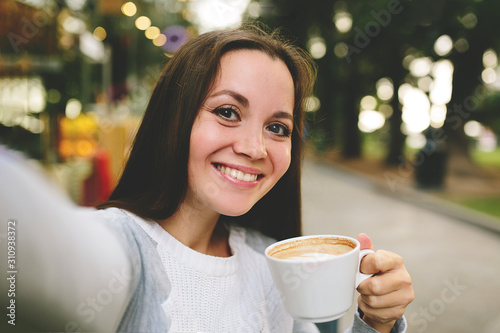 Young beautiful girl with a coffe taking and makes selfie in street cafe.