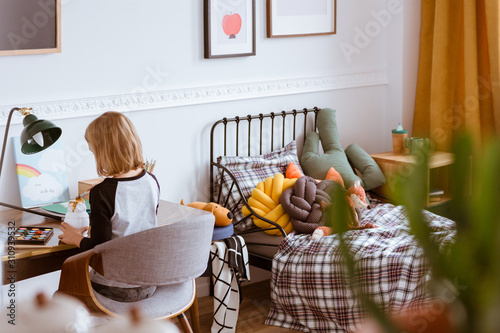 Cute little girl sitting at desk making homework in her stylish vintage bedroom with workspace