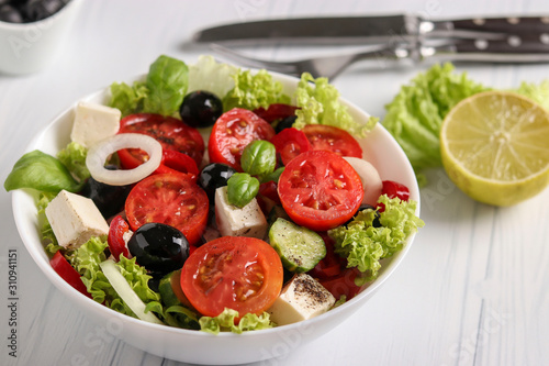 Healthy Greek salad of green lettuce, cherry tomato, onion, pepper, feta cheese, black olives, basil, cucumbers, with olive oil and lemon juice, Closeup
