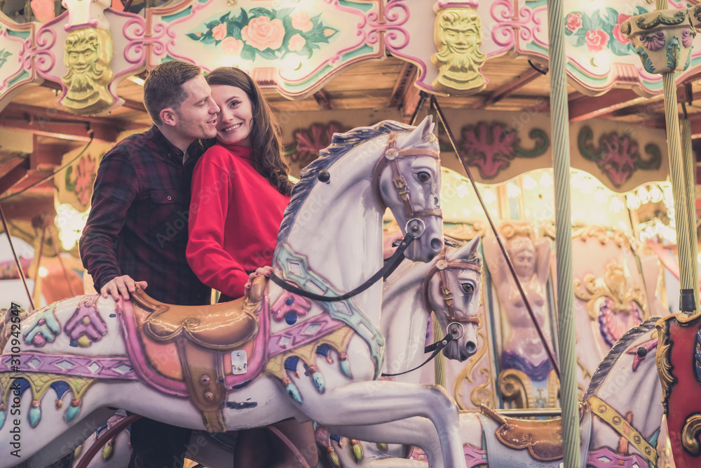 romantic couple taking a moment to kiss while riding horses on carousel