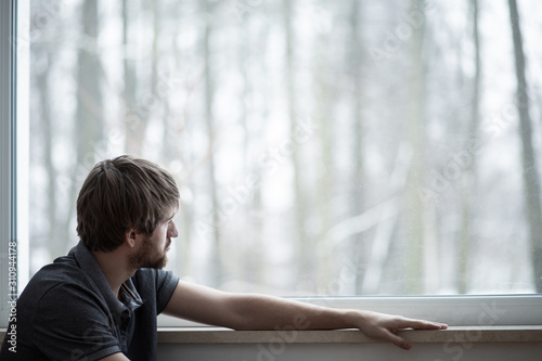 Canvas Print Young man sitting on the floor of living room with big window