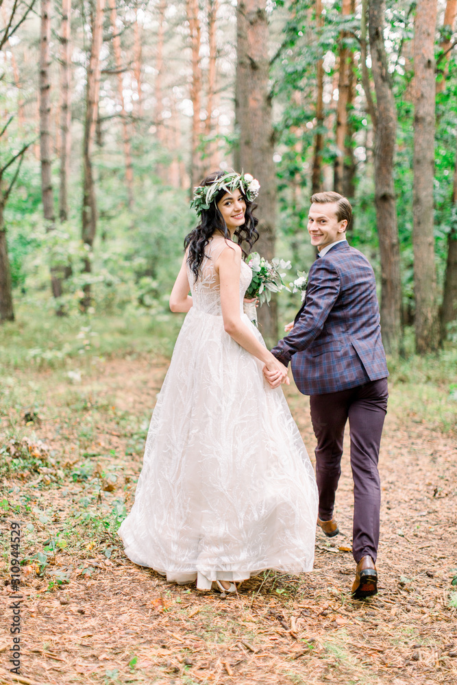 Bride and groom running in the forest.