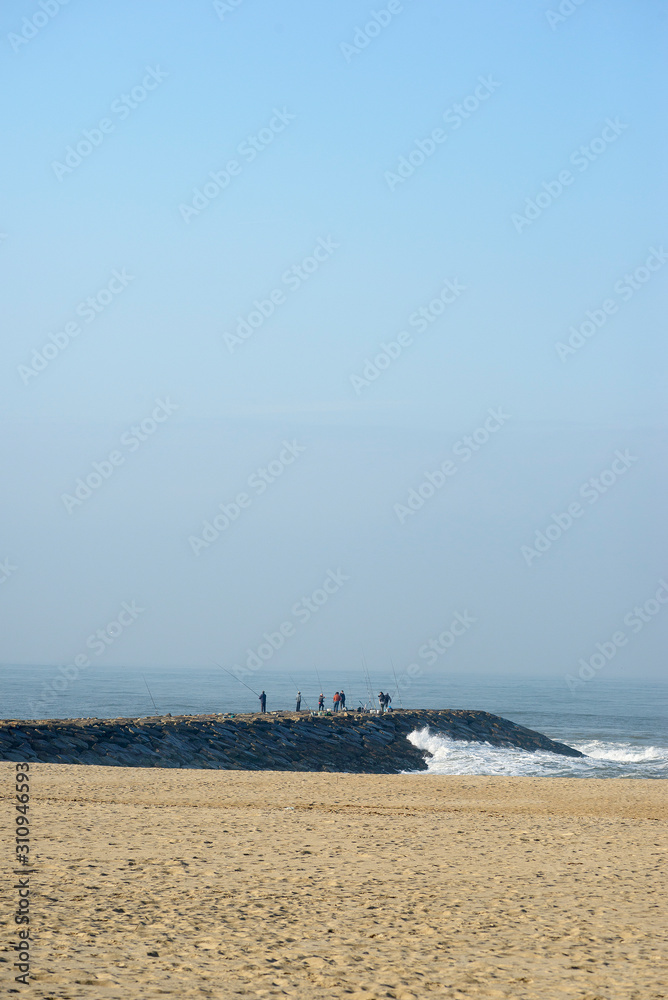 people fishing on the breakwater of a beach in Portugal with sand and blue sky in the Atlantic Ocean