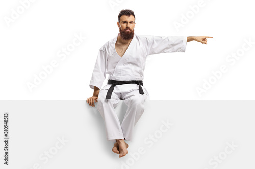 Fotografie Man in karate kimono with black belt sitting on a blank panel and pointing to on