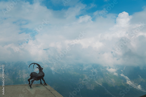 Statue of a goat on the slope of the Alps. Ahead of the mountain peaks in the snow. Clouds and fog. Austria photo