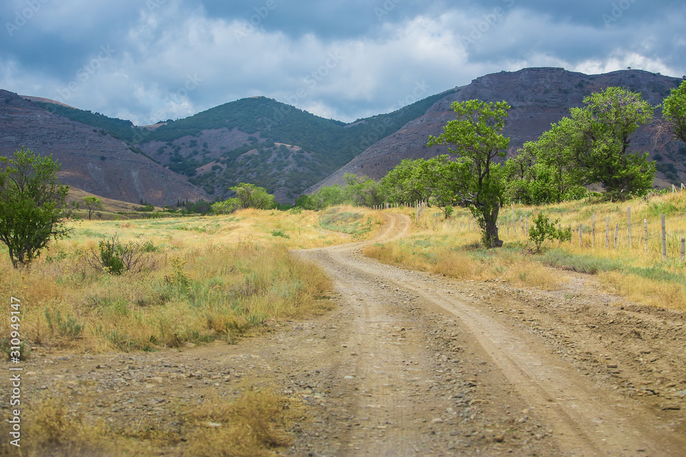 dirt road towards the mountains and cloudy sky