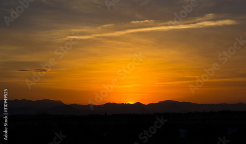 View of golden sky with the mountain silhouette in the time of lovely sunset over a city.
