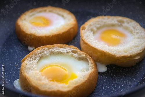 three eggs baked in round buns in a dark pan top view close-up