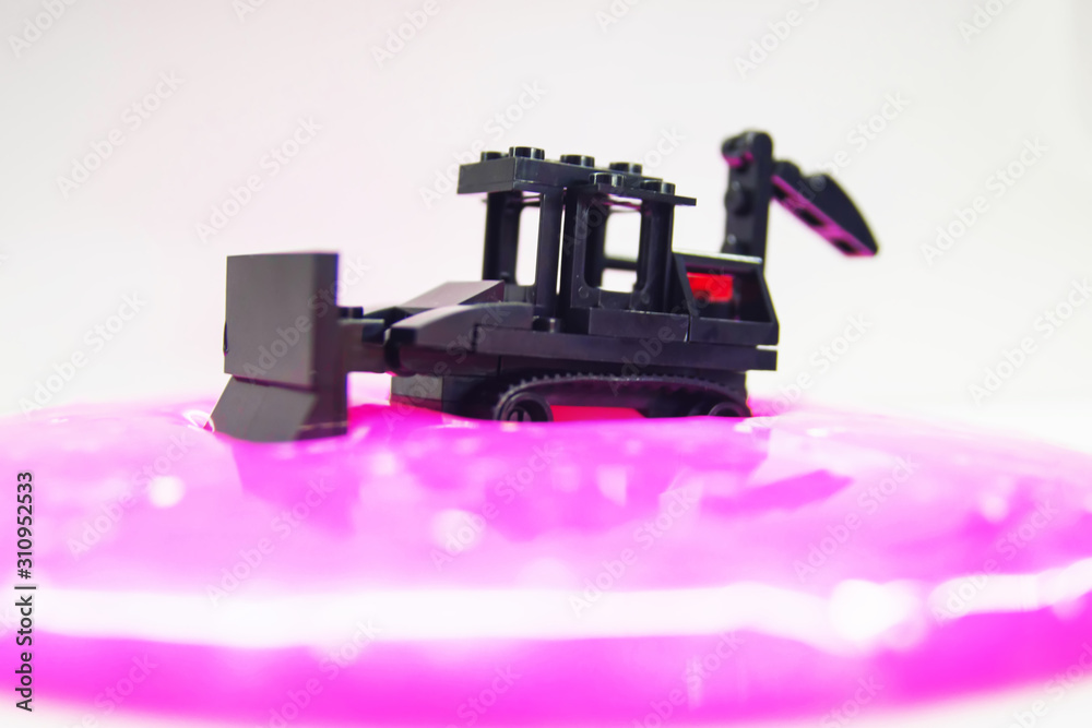 Naklejka premium black toy bulldozer from designer cubes removes pink gel with glitter on a white background