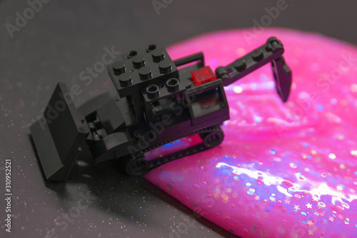black toy bulldozer from designer cubes removes pink gel with glitter on a black background
