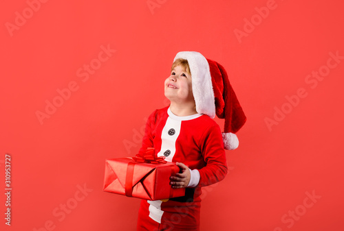Christmas children. Little kids celebrating Christmas. Child with Christmas present. Happy boy in Santa costume holds present. New year kid. Funny wintertime. Santa helper holds box with present gift.