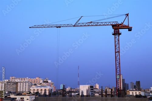 Red steel construction crane with building in city background and blue sky light sunset 