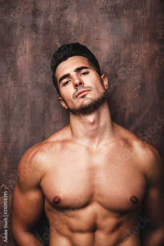 Portrait of handsome young man with stylish haircut posing over rusty wall background. Perfect hair & skin. Close up. Studio shot