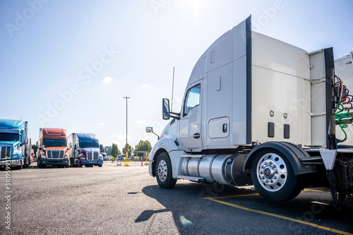 Fototapeta Naklejka Na Ścianę i Meble -  Classic bonnet big rig white semi truck tractor stand on the truck stop parking lot across another semi trucks standing in row for truck drivers rest