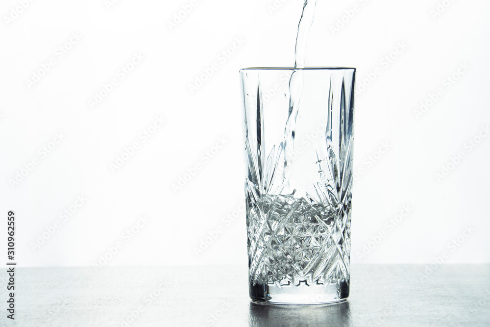 Water is poured into a crystal glass on a white background. Water is poured into a crystal glass on a white background.