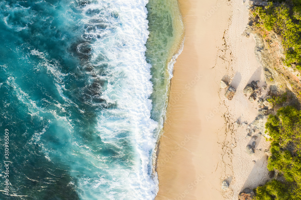 View from above, stunning aerial view of a rocky shore with a beautiful beach bathed by a rough sea during sunset, Nyang Nyang Beach (Pantai Nyang Nyang), South Bali, Indonesia.